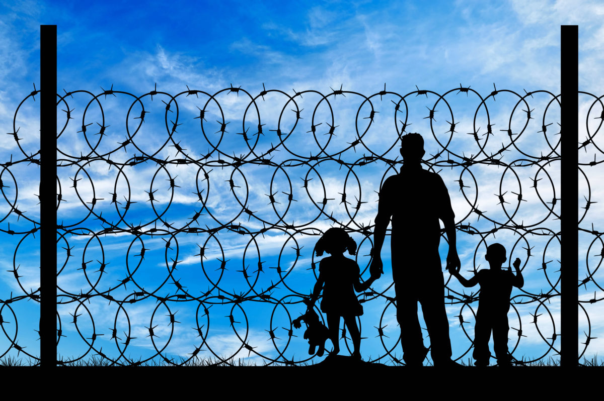 Silhouette of a family with children of refugees and fence with barbed wire on the background of the beautiful sky